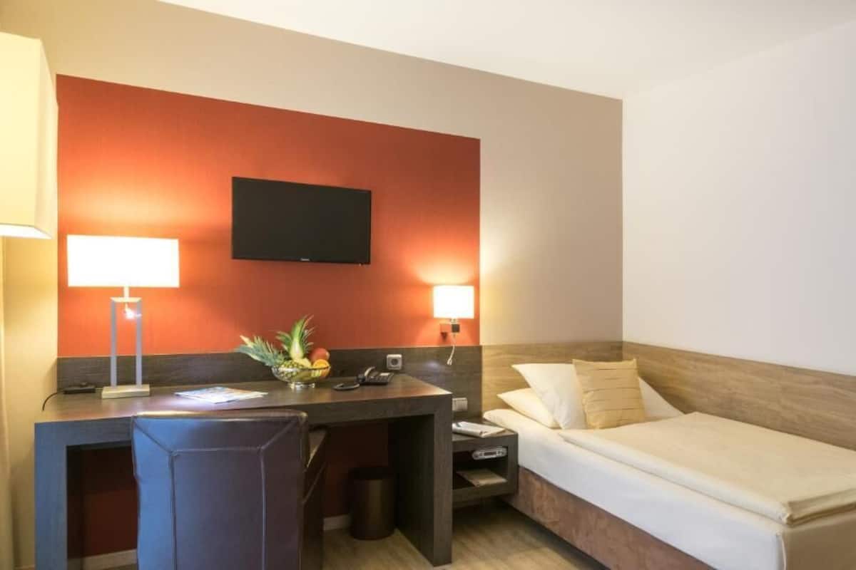 A hotel room with a desk, chair, bed, TV, and two bedside lamps.