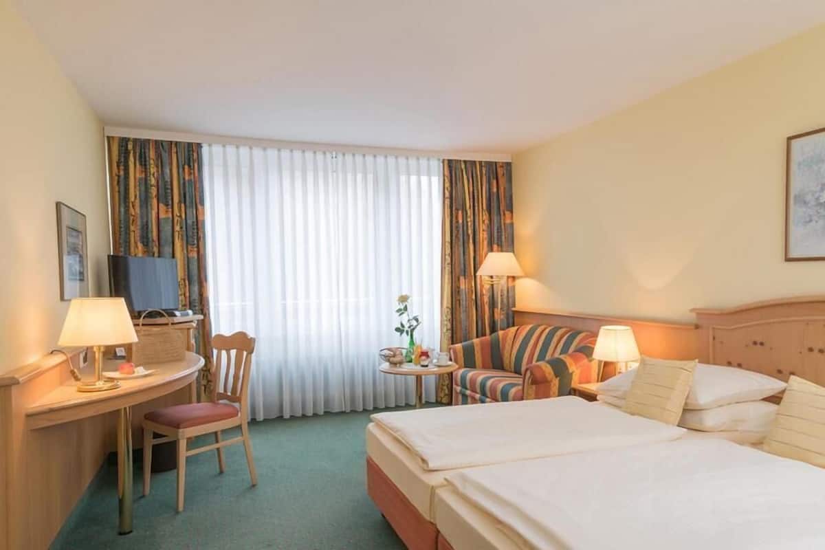 A hotel room with a bed, a desk, a chair, a sofa, and a television.