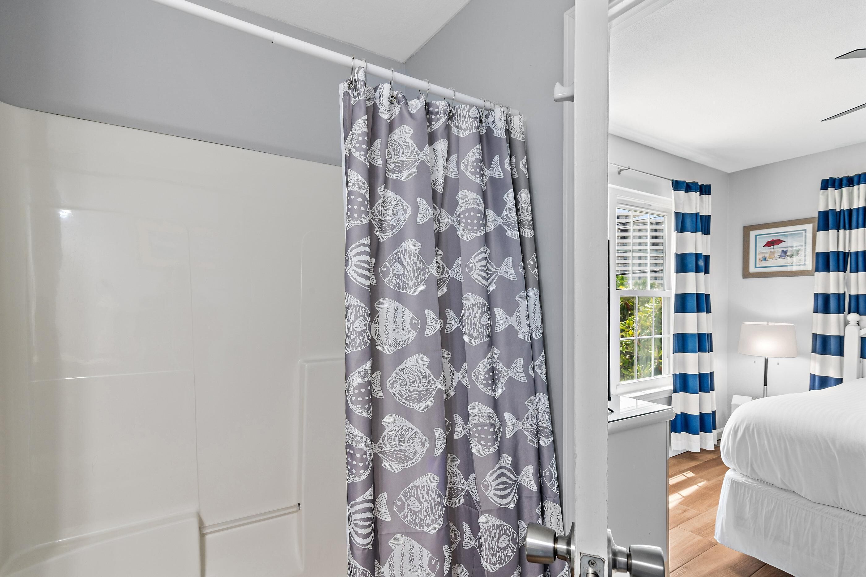 A bathroom with a shower curtain featuring fish patterns, a white bathtub, and a window with blue and white curtains.