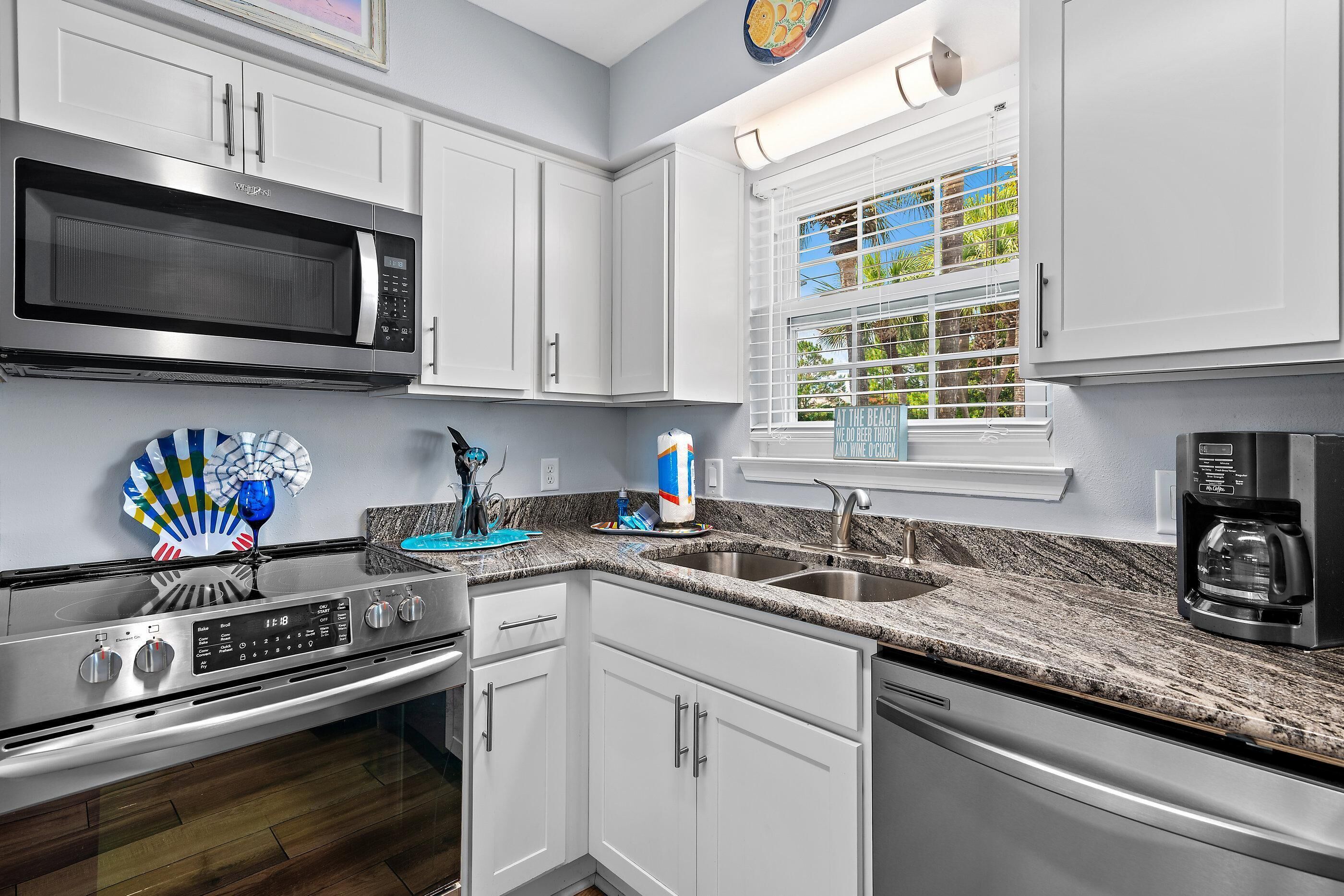 A modern kitchen with white cabinets, a stainless steel microwave, a gas stove, a sink, and a coffee maker.