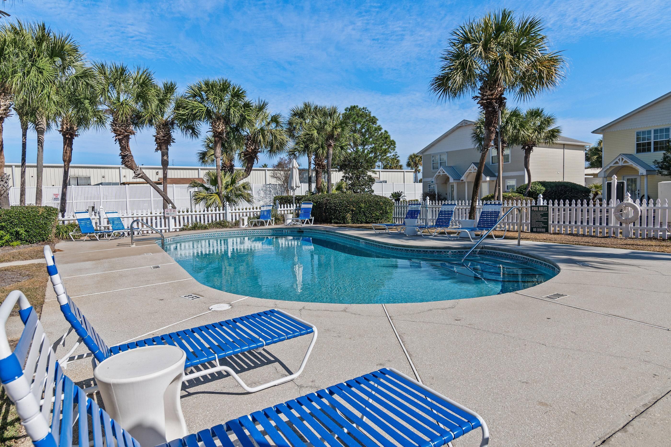 A swimming pool with blue lounge chairs and palm trees.