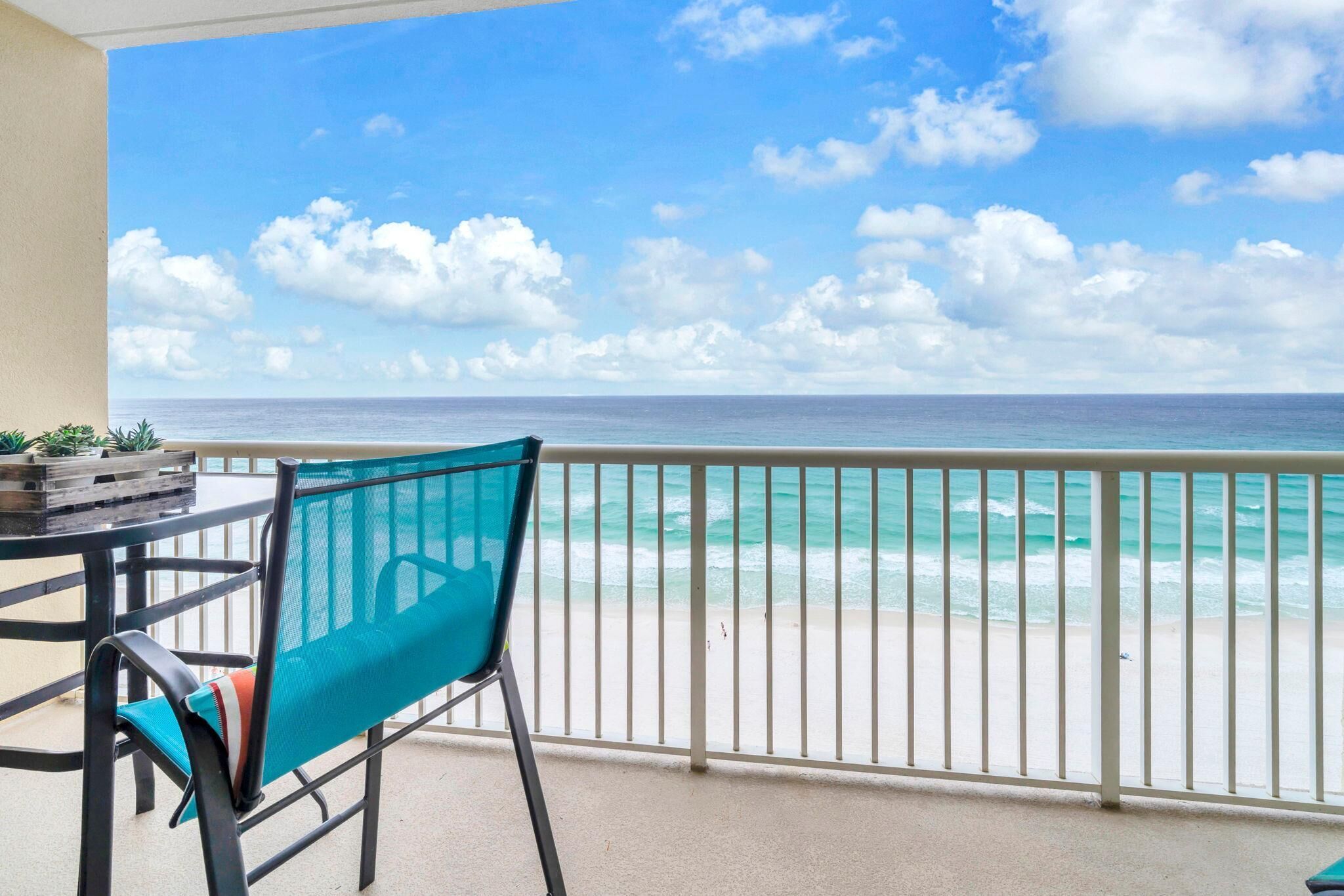A balcony with a view of the ocean, a chair, and a table with a plant.
