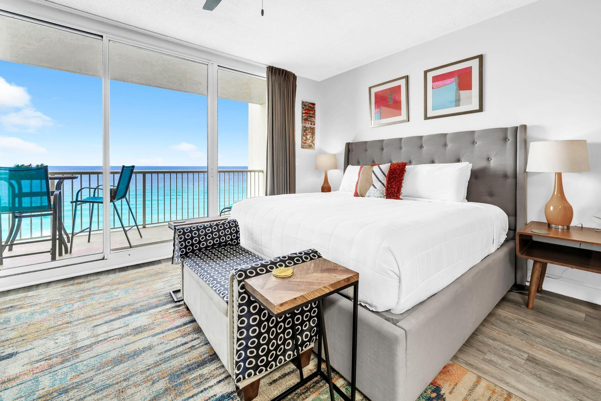 A hotel room with a bed, a small table, a chair, a nightstand, and a view of the ocean.