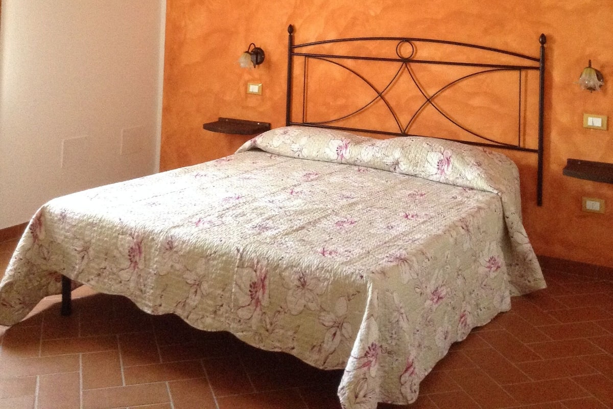 Un dormitorio con cama, vigas de madera en el techo y suelo de baldosas.