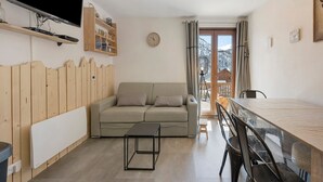 Una sala de estar moderna con un sofá, un televisor montado en la pared, un panel de pared de madera, una mesa de comedor con sillas y vistas a las montañas desde la ventana.