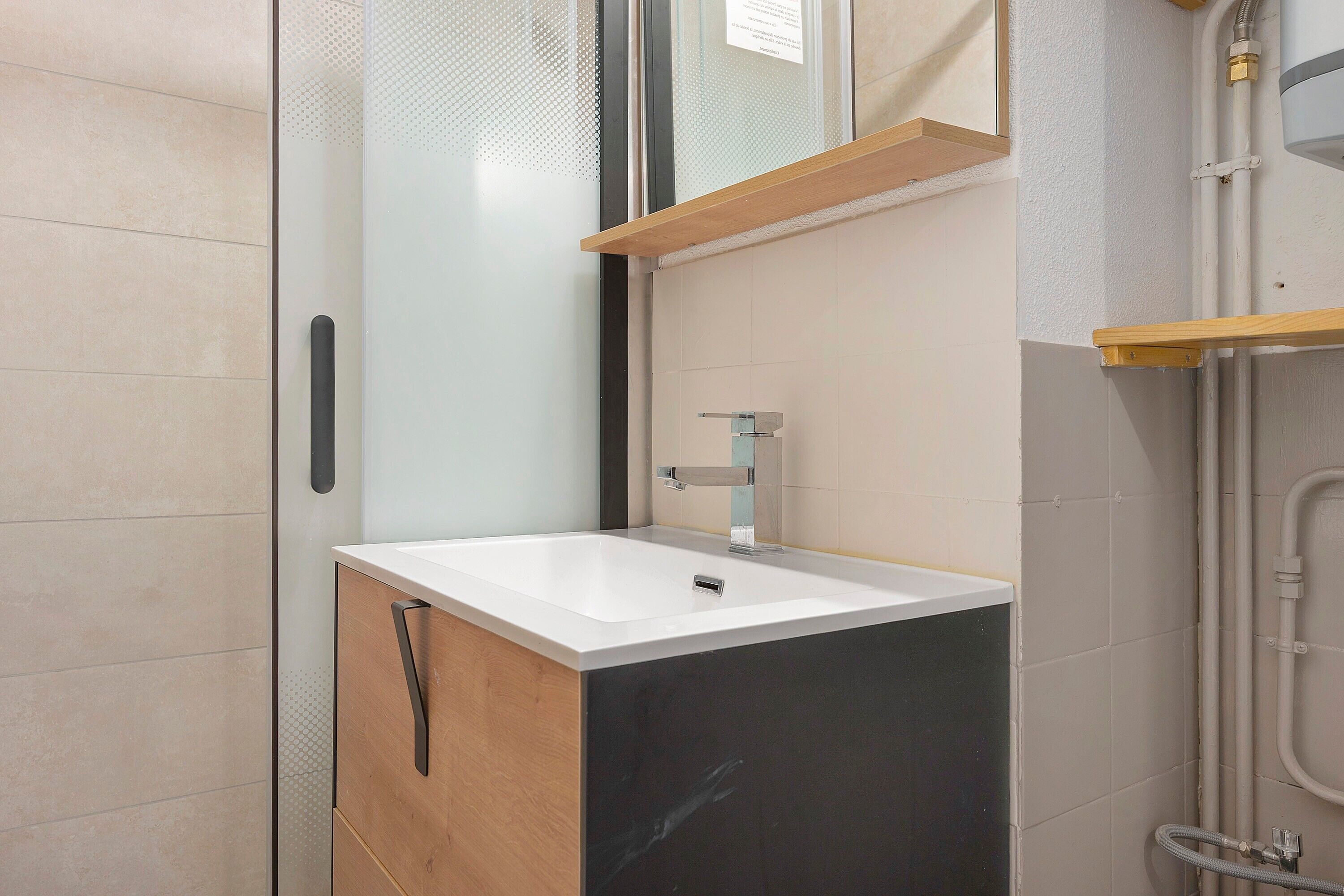 Een badkamer met een witte wastafel, een spiegel en een douchehoek.