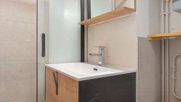 Een badkamer met een witte wastafel, een spiegel en een douchehoek.