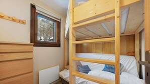 Dormitorio con literas, ventana, paredes de madera y radiador.