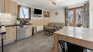 Una cocina moderna con armarios de madera, lavavajillas, televisor y comedor con mesa y sillas.