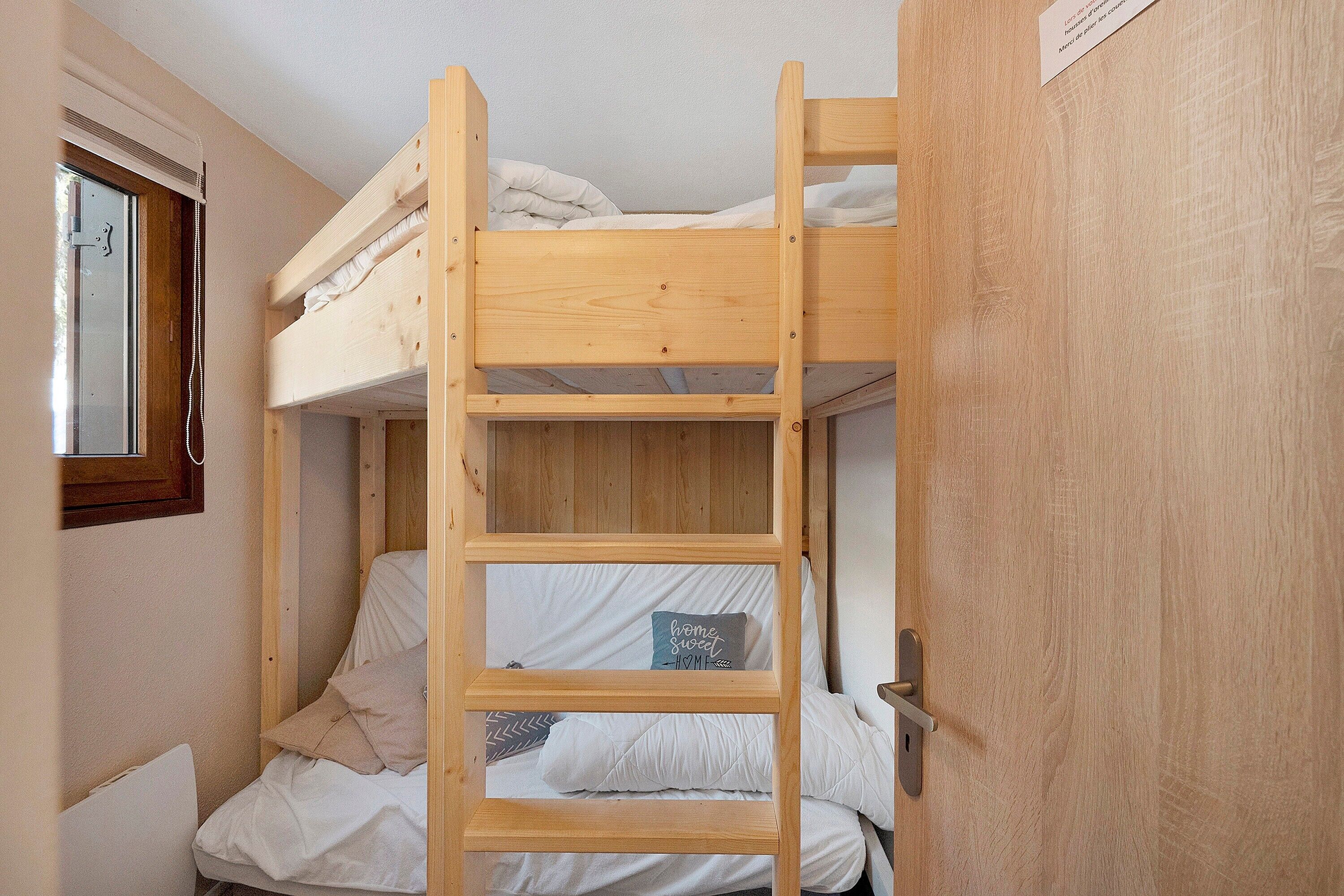 Un lit superposé avec une échelle, une petite fenêtre et une porte.
