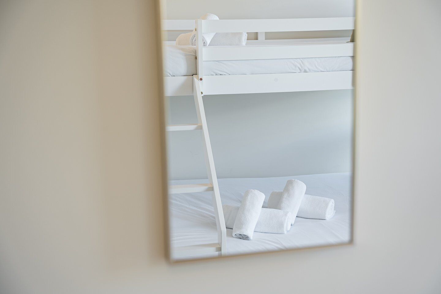 A bunk bed with white bedding and rolled towels on the lower bunk.