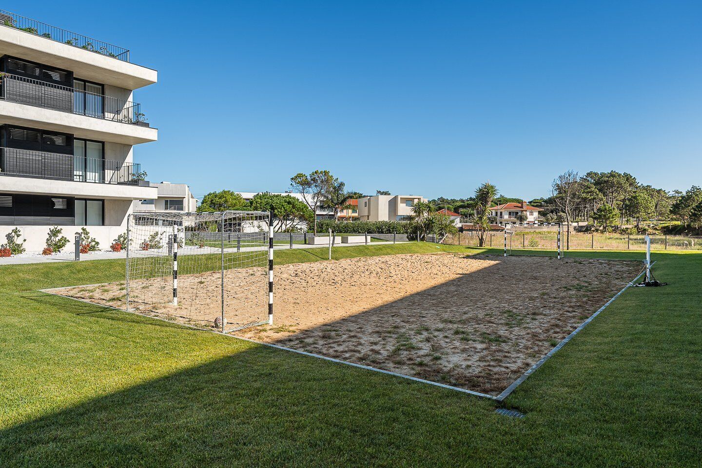 Una cancha deportiva con una red, rodeada de césped y un edificio con balcones.