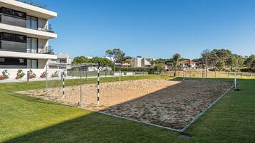 Una cancha deportiva con una red, rodeada de césped y un edificio con balcones.