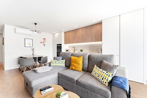 A modern living room with a grey sectional sofa, a round coffee table, and a dining area with a small table and chairs. - GuestReady - Apúlia coastal retreat (Apúlia e Fão)