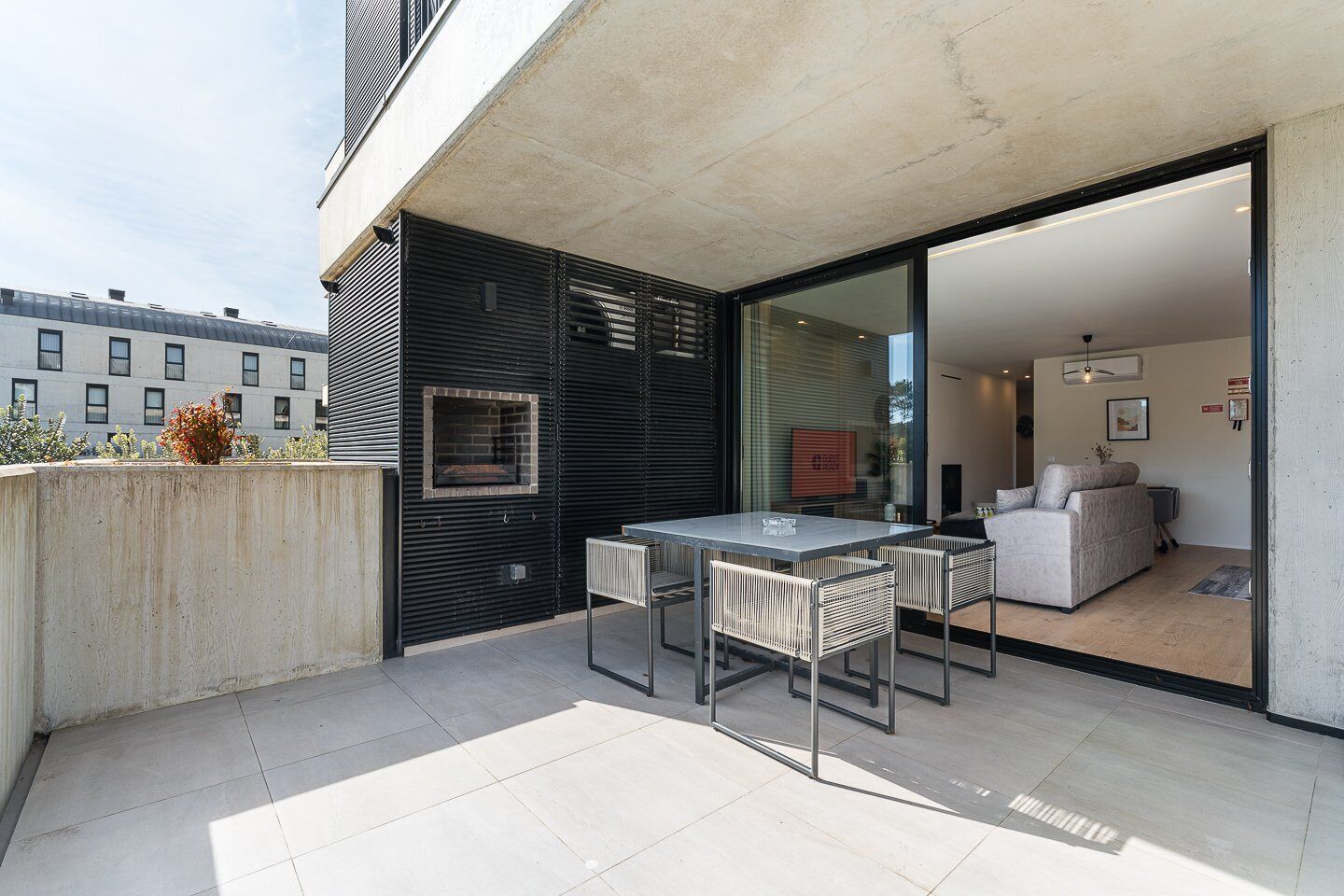 A modern outdoor patio with a glass door leading to a living area, a built-in grill, and a seating arrangement.