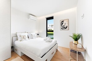 A modern bedroom with a large bed, a bedside table with a plant, and a view of a building through an open door. - GuestReady - Apúlia coastal retreat (Apúlia e Fão)