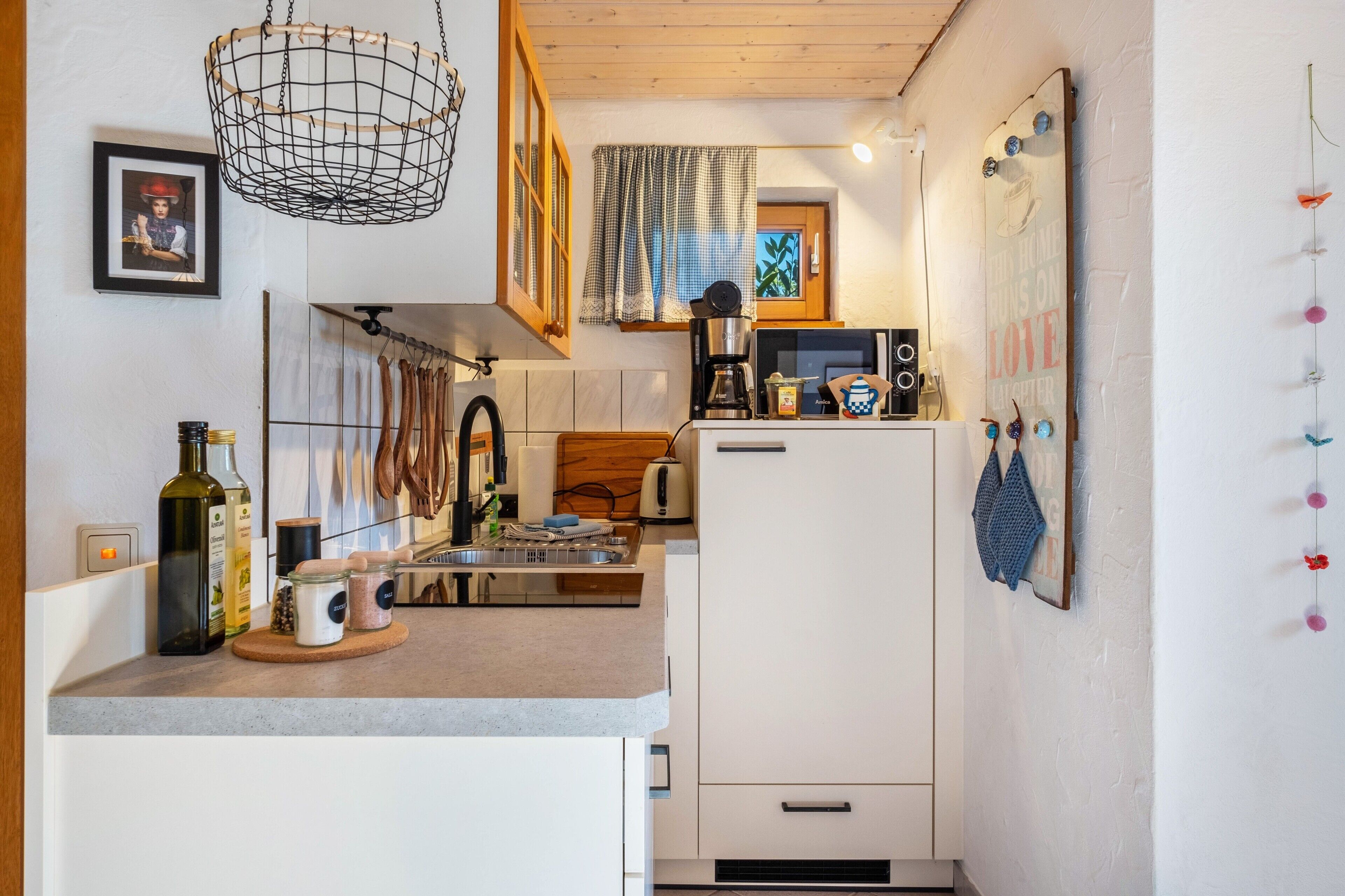 A compact kitchen with a microwave, coffee maker, and wooden utensils.