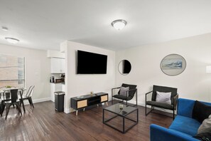 A modern living room with a flat-screen TV, a coffee table, a blue sofa, and a dining area with a table and chairs. - Modern 1BR Retreat in Vibrant Austin w/ AC (Austin)