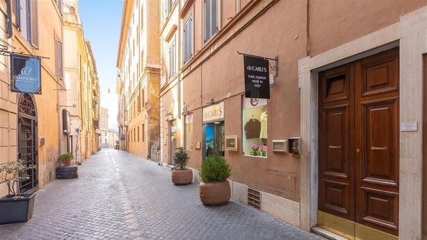A cobblestone street with buildings on either side, featuring storefronts with signs for 'deCARLI'S' and 'OLFATTORIO'. - Vittoria RiR Collection (Rome)