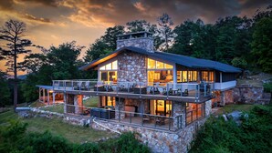 A stone house with a balcony and large windows, surrounded by trees.