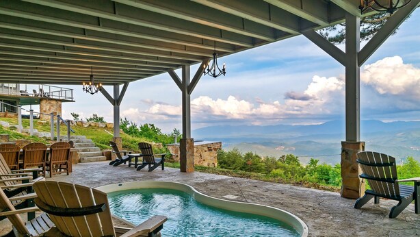 A pool area with lounge chairs, a stone deck, and a view of mountains.