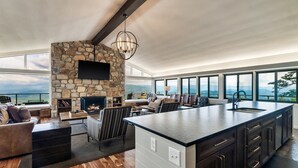 A modern kitchen with a stone fireplace, large windows, and a view of the mountains.