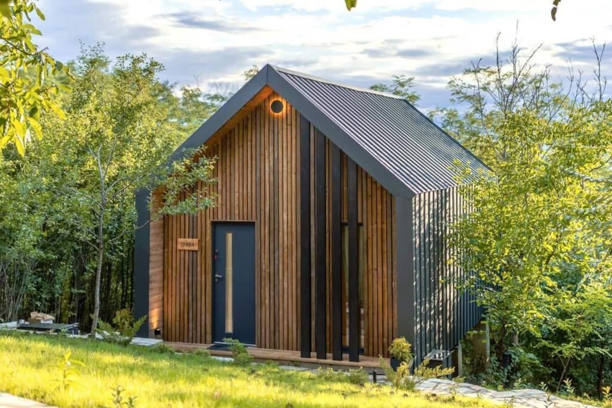 Een modern, rustiek vakantiehuisje met een schuin dak, houten gevelbekleding en een voordeur met een naambordje.