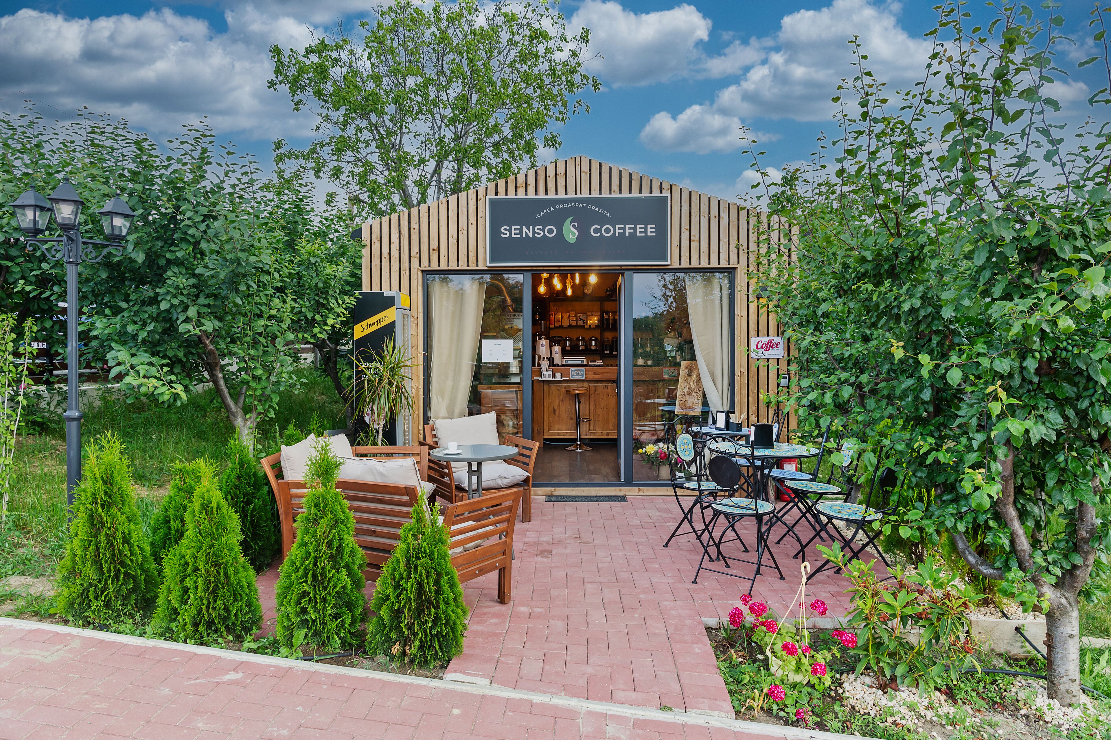 Un rincón acogedor al aire libre con mobiliario de madera y la entrada a una cafetería.
