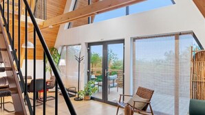 Un interior espacioso con una escalera de madera, un comedor y una zona de estar con vistas a través de grandes puertas correderas de vidrio.