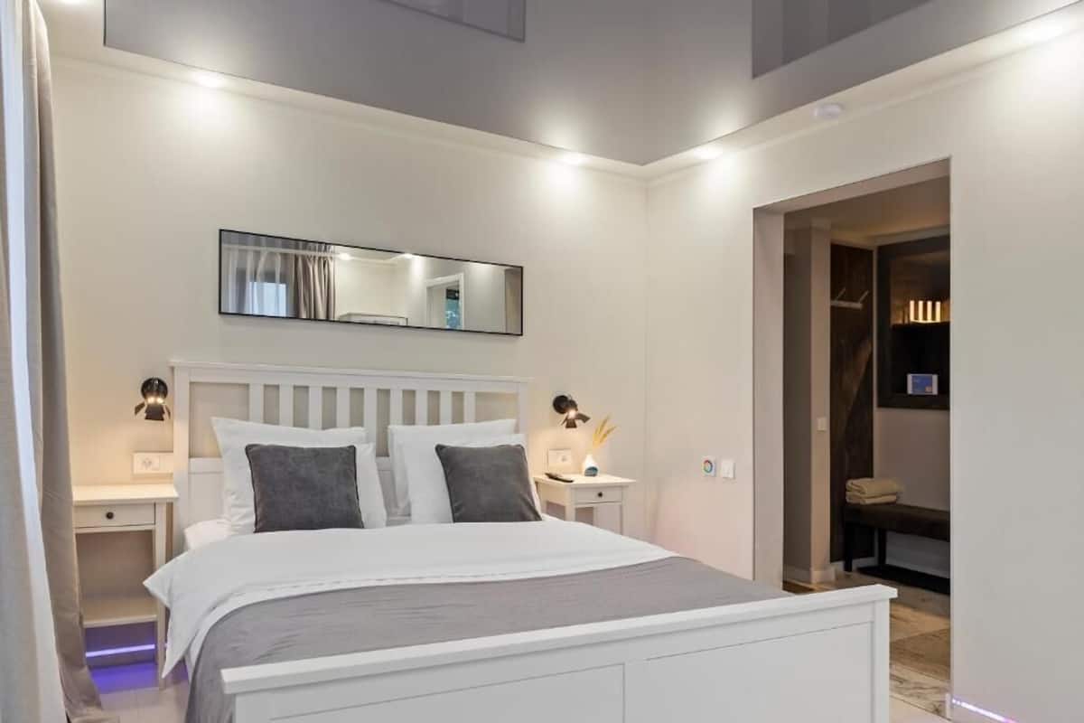 Een moderne slaapkamer met een wit bed, nachtkastjes, een spiegel en een inloopkast.