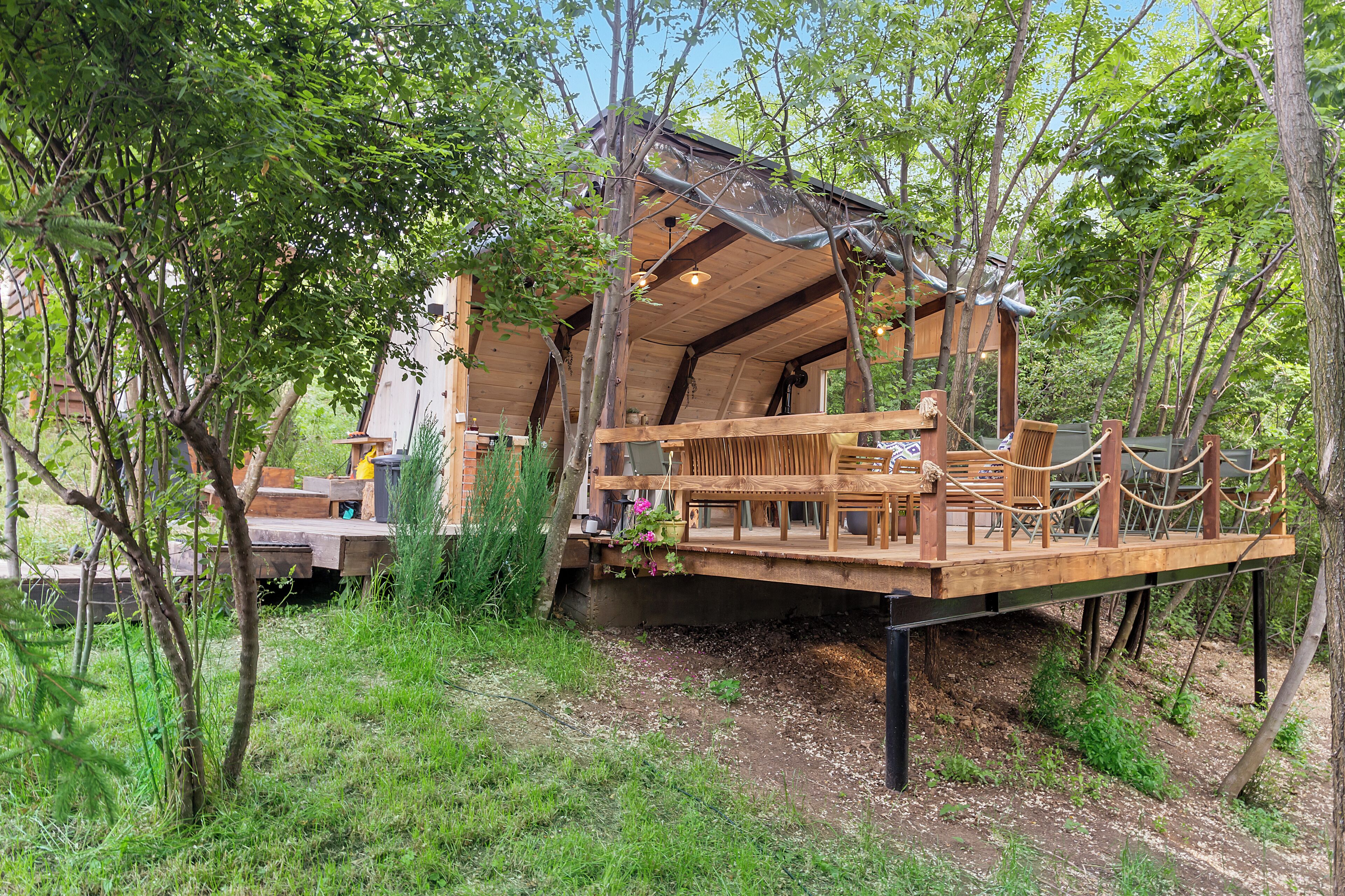A wooden cabin with a deck, surrounded by trees.