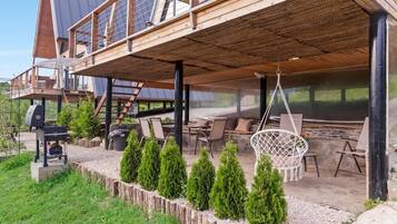 A modern wooden house with a covered patio area, outdoor seating, and a barbecue grill.