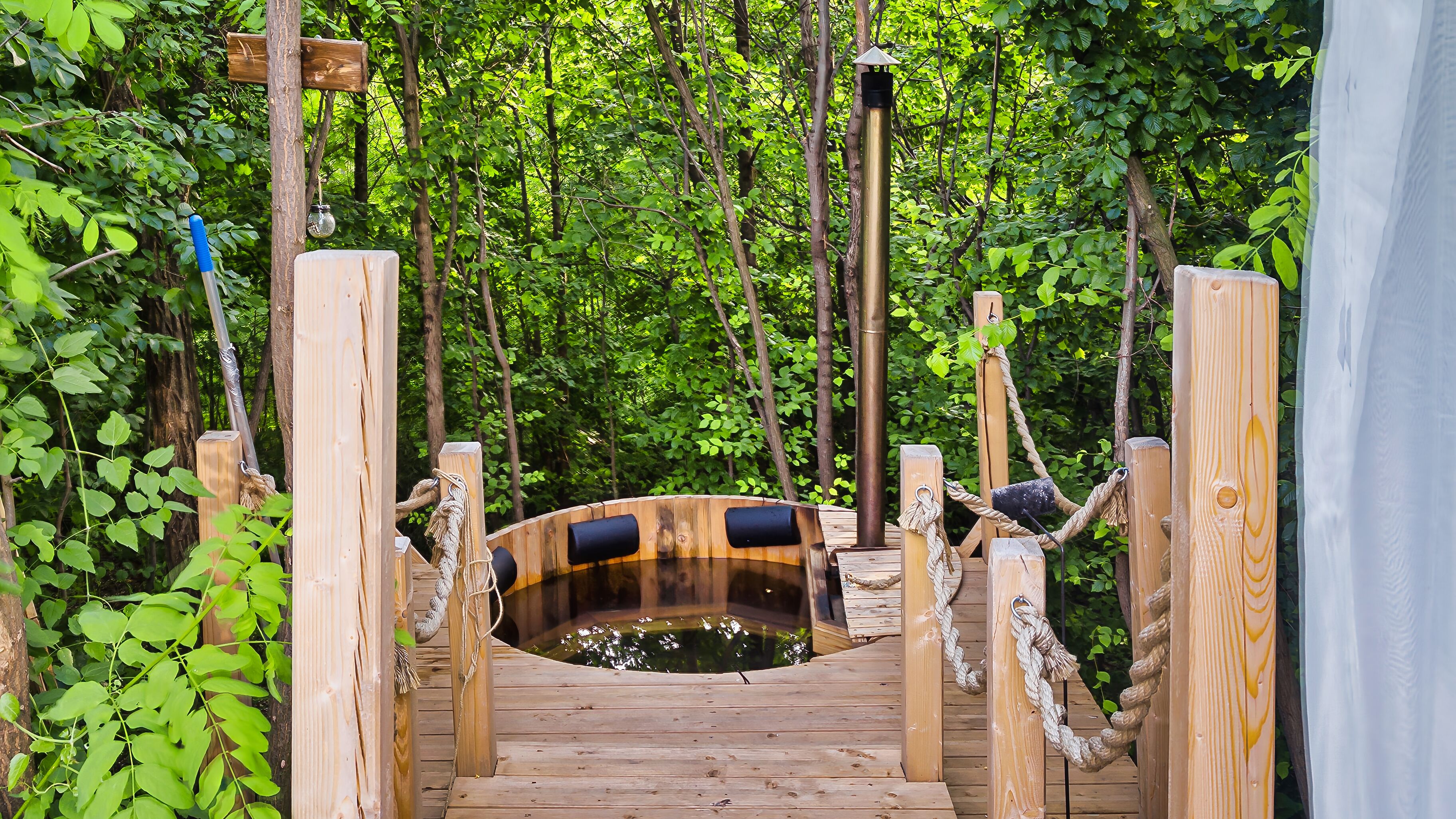 A wooden bridge leading to a hot tub surrounded by lush greenery.