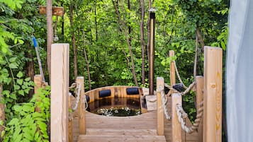 A wooden bridge leading to a hot tub surrounded by lush greenery.