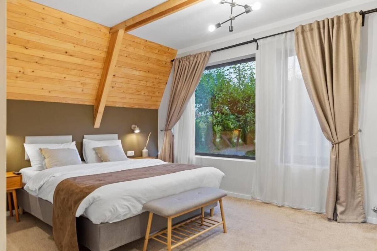 Een slaapkamer met een bed, een bankje, nachtkastjes en gordijnen.