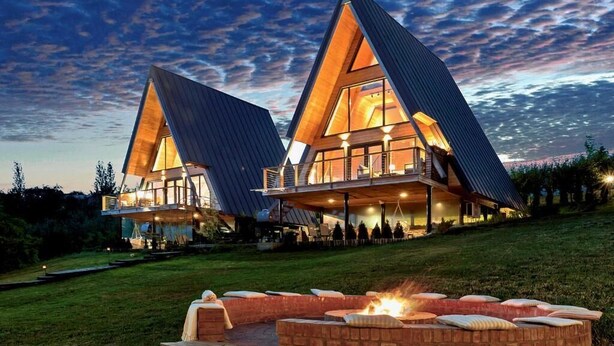 Un edificio moderno de forma triangular con grandes ventanales y un interior bien iluminado, ubicado en una ladera cubierta de césped con un hogar a la vista.