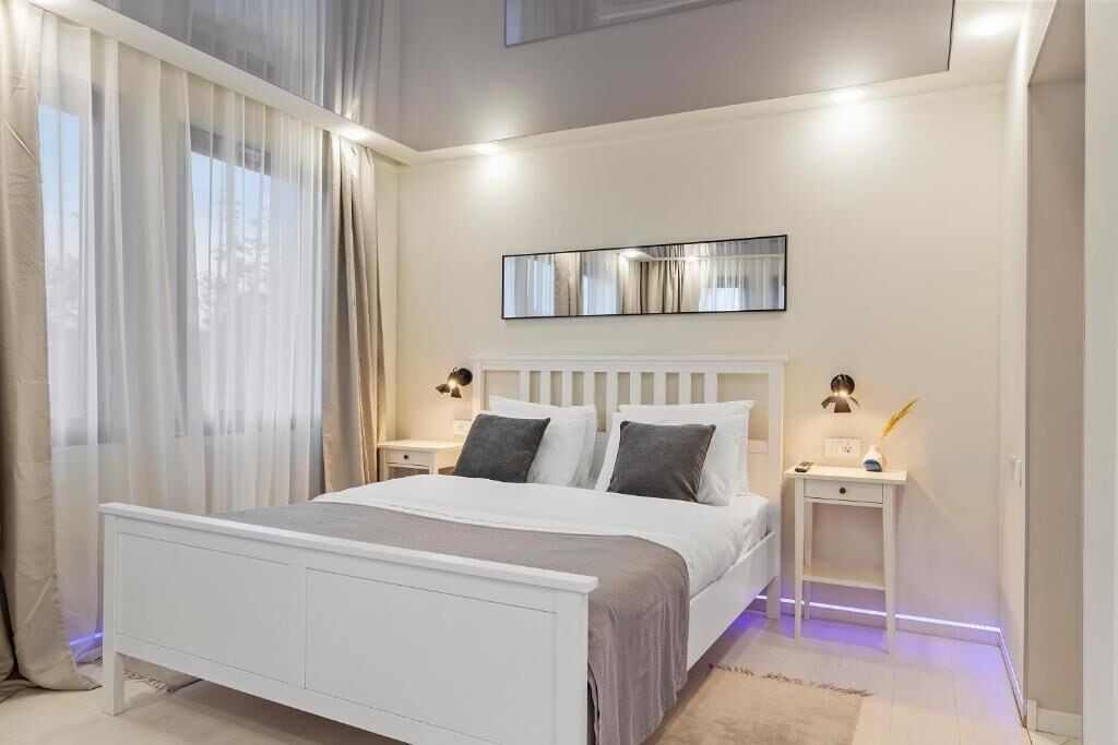 Un dormitorio moderno con una cama blanca, dos mesitas de noche y un espejo grande en la pared.