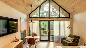Un interior moderno con techo de madera, un ventanal grande, una zona de comedor y un sofá verde.