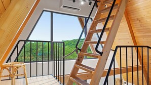 Interior de madera con una escalera de madera, una silla de mimbre y un gran ventanal con vistas a zonas verdes.