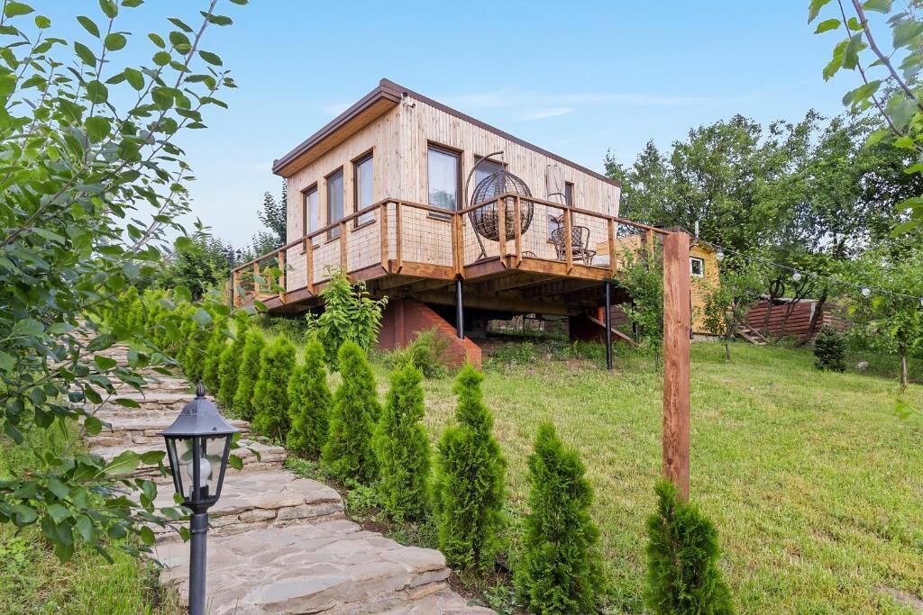Una casa de madera con balcón, rodeada por un camino de piedra y pequeños árboles.
