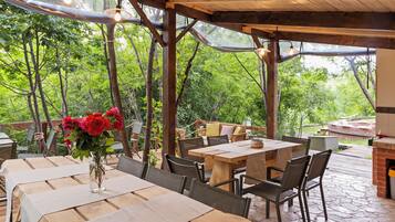 An outdoor dining area with wooden tables and chairs, surrounded by a wooden pergola with hanging lights.