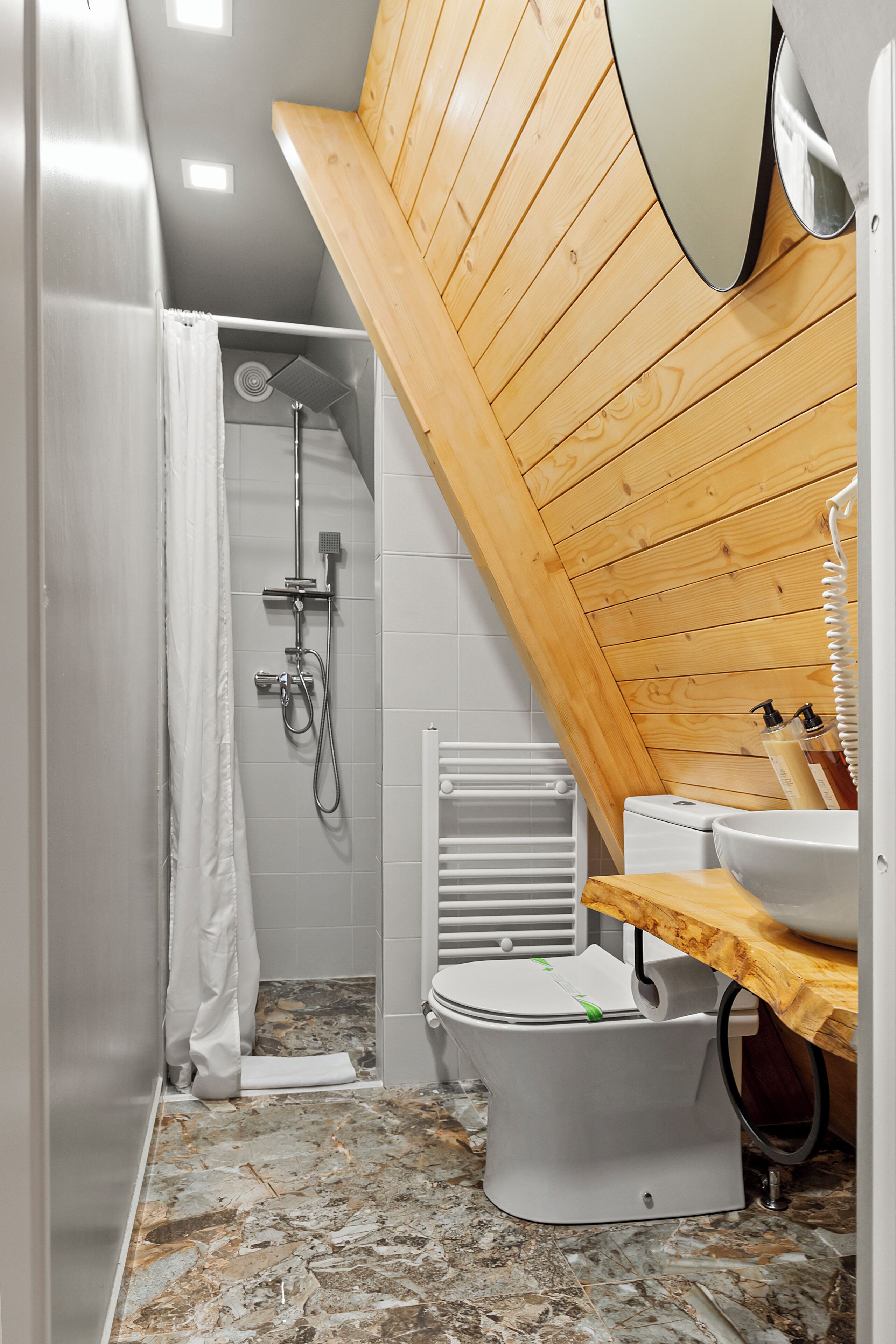 Un baño pequeño con ducha, inodoro y lavamanos, con paneles de madera y suelo de mármol.