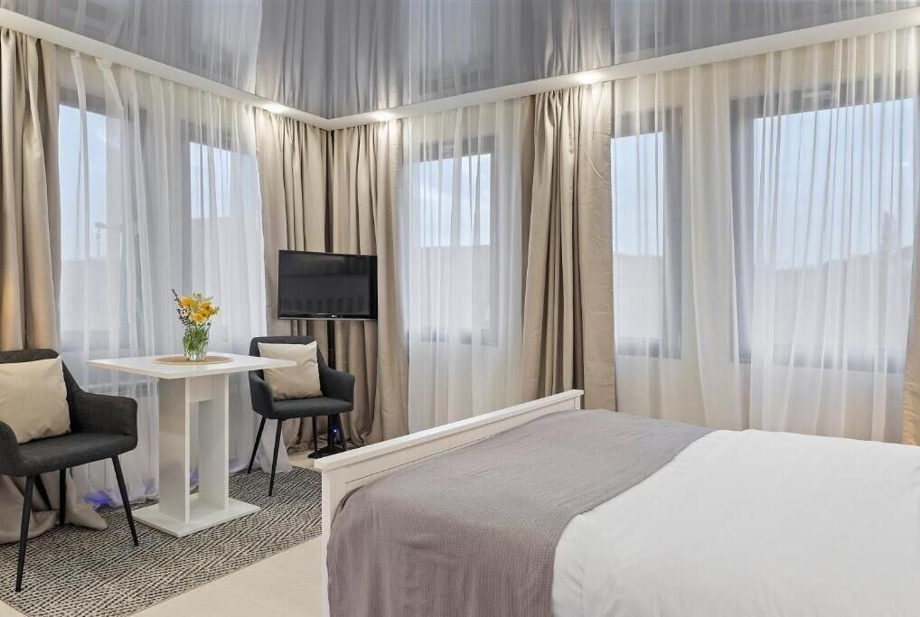 Una camera d'albergo moderna con un letto grande, una scrivania con due sedie, una TV a schermo piatto e tende leggere.