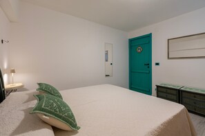 Een slaapkamer met een bed, een blauwgroene deur, een spiegel en een dressoir.