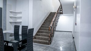 Un interior moderno con una escalera, un área de comedor con una mesa de vidrio y sillas negras, y paredes blancas.