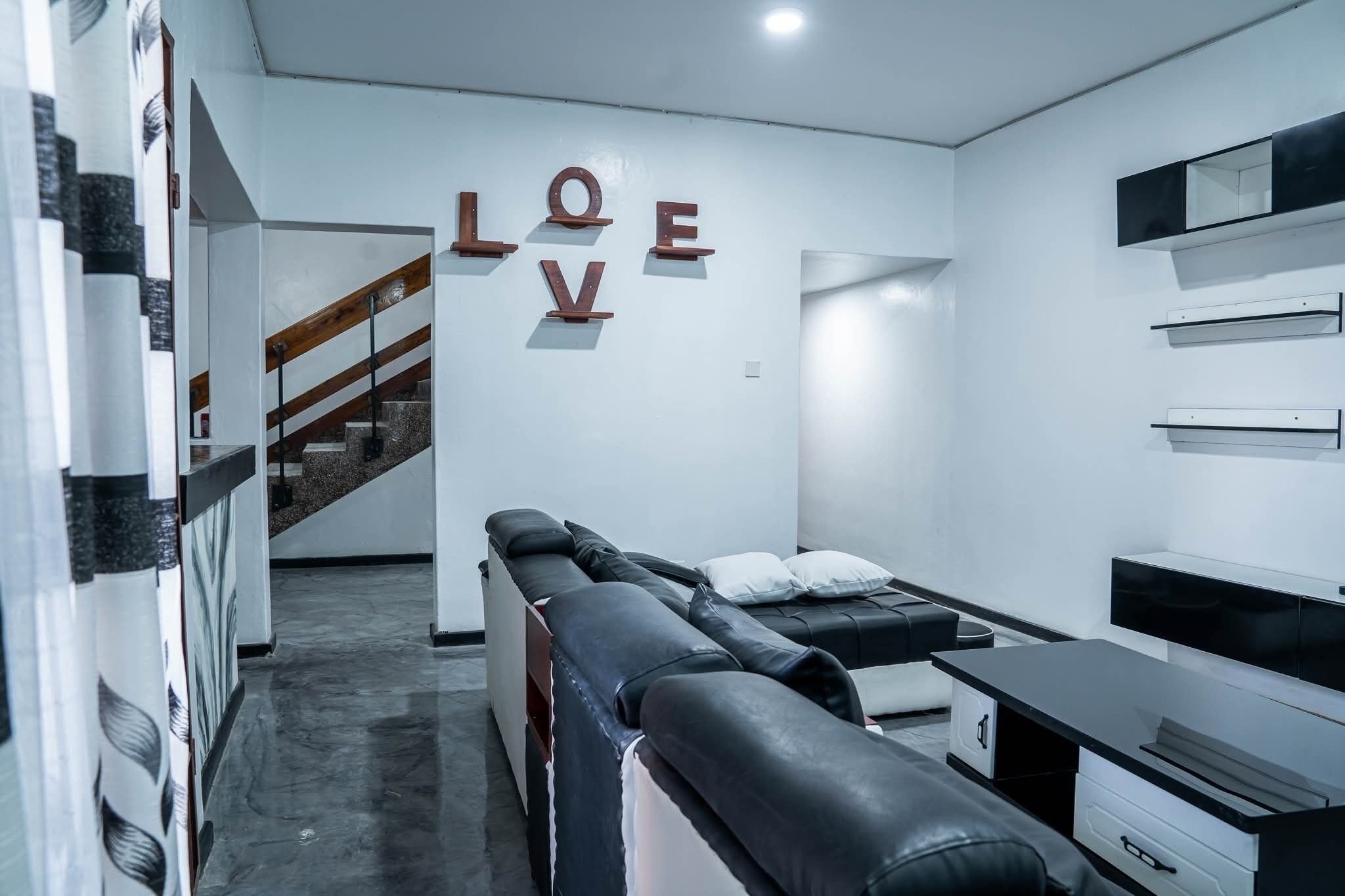 Un intérieur moderne avec un canapé en cuir noir, un escalier et une étagère murale sur laquelle est inscrit le mot « AMOUR ».