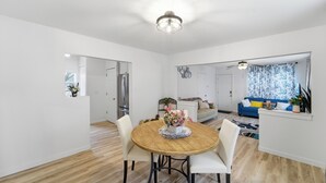 Amplia sala de estar con una mesa de comedor de madera, sillas blancas, un sofá azul y una cortina estampada.