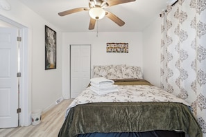 A bedroom with a bed, a ceiling fan, a door, and a wall with a patterned curtain.