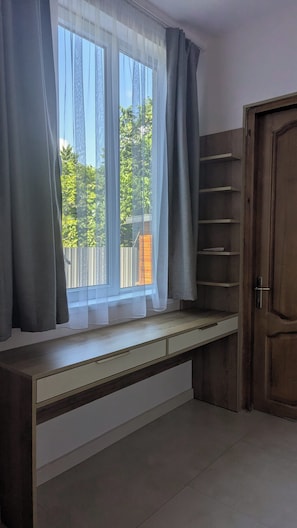 A room with a built-in bench under a window, a wooden door, and a view of greenery outside.