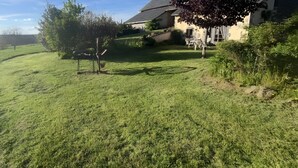Eine grüne Wiese mit einem Haus, einem Baum und einem Zaun.